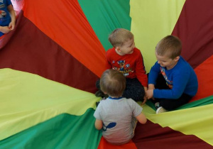 Zabawa z chustą – troje dzieci siedzi na chuście pozostałe kręcą chustą.